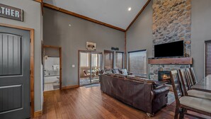Un amplio salón con chimenea de piedra, sofá de cuero y una zona de comedor con sillas de madera.