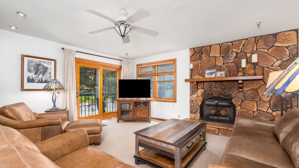 A living room with leather sofas, a wooden coffee table, a stone fireplace, a flat-screen TV, and a ceiling fan. - Family Friendly Condo- Walk to Main Street and Town Lift (Park City)