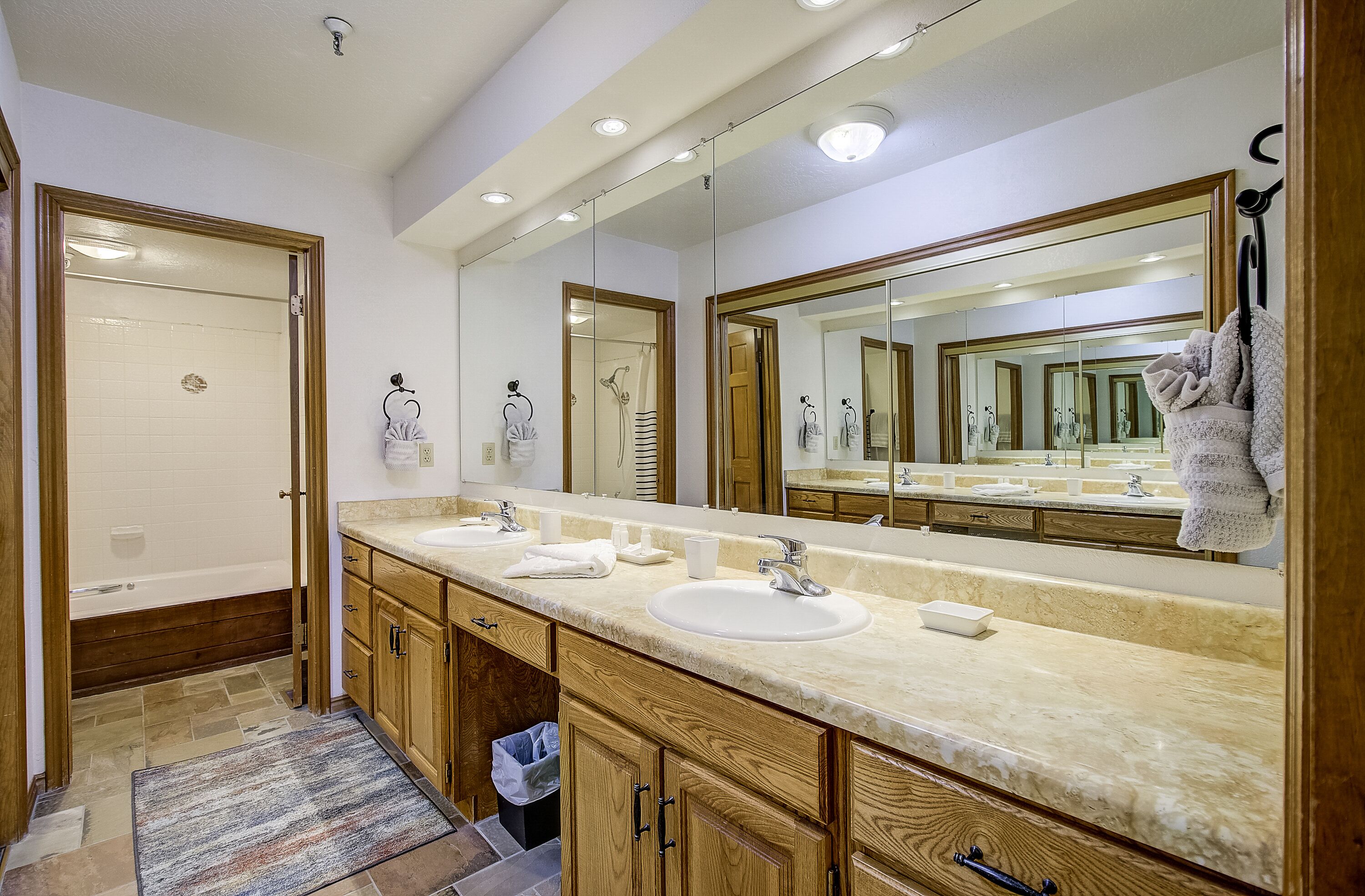 A bathroom with a double sink vanity, wooden cabinets, a large mirror, and a shower area.