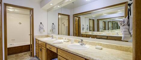 A bathroom with a double sink vanity, wooden cabinets, a large mirror, and a shower area.