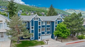A two-story building with a blue exterior and a garage door. It is surrounded by trees and located near a road with a bike lane. - Family Friendly Condo- Walk to Main Street and Town Lift (Park City)