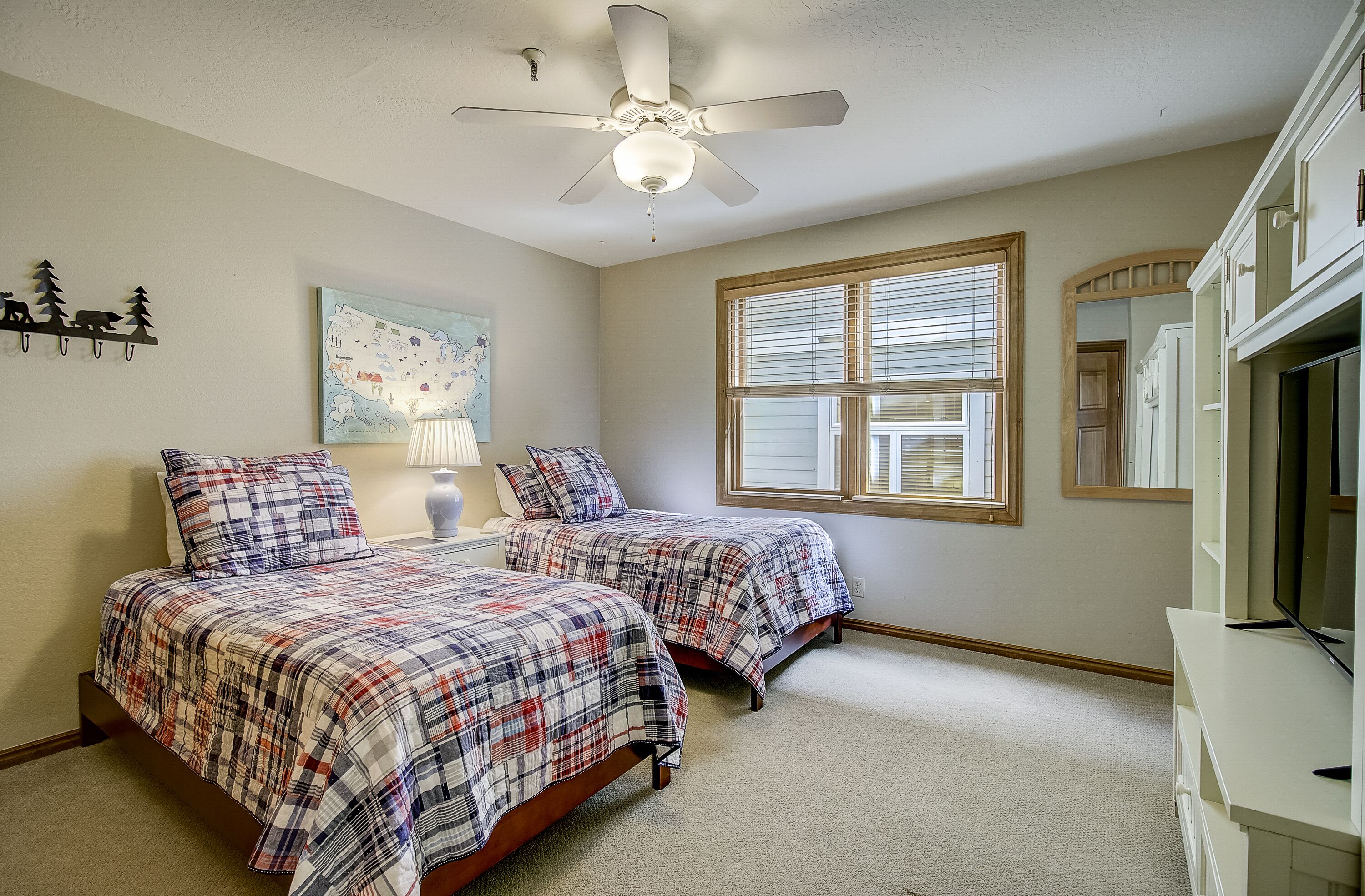 A bedroom with two beds, a ceiling fan, a window with blinds, a lamp, and a TV on a stand.