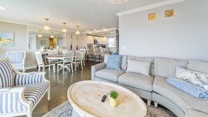 Ein geräumiges Wohnzimmer mit grauem Sofa, gestreiften Sesseln, einem Holztisch und einem Essbereich mit weißem Tisch und Stühlen.
