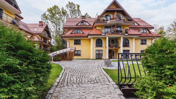 Un grand bâtiment jaune, avec une allée pavée et un portail en métal.