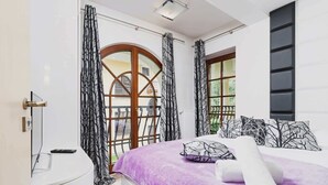 Une chambre à coucher avec un lit, une table de chevet, une fenêtre avec des rideaux et une vue sur l’extérieur.