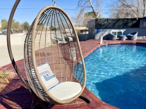 Una silla de mimbre con cojín junto a una piscina.