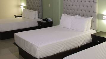 A hotel room with two beds, each with a tufted headboard, white bedding, and bedside tables with lamps.