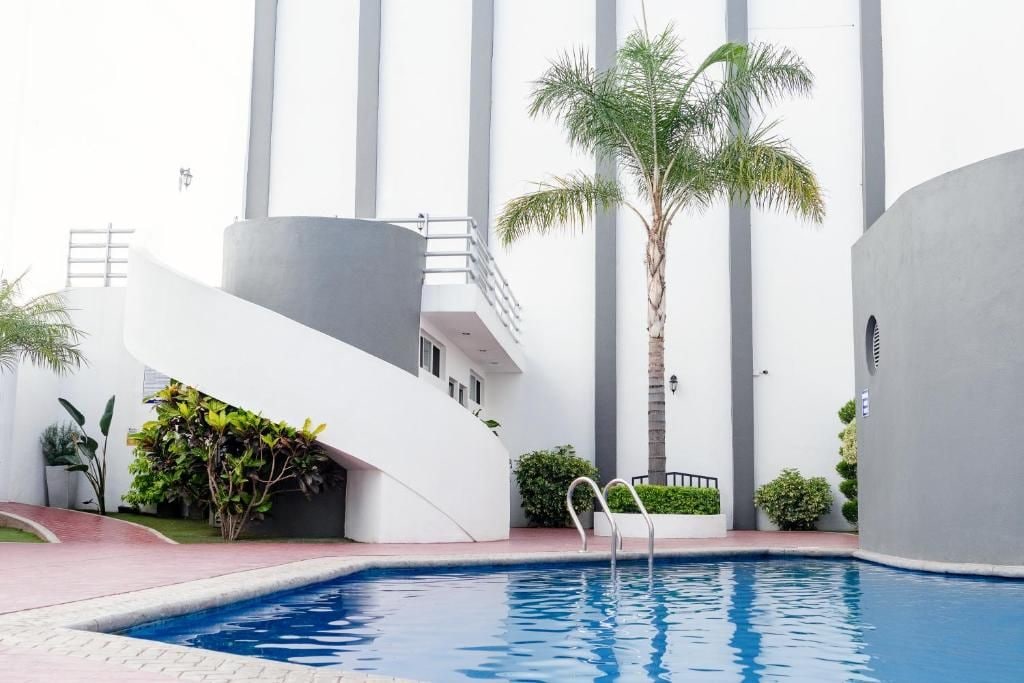Un edificio moderno con piscina, palmeras y una estructura blanca curva.