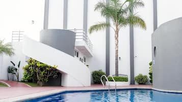 Un edificio moderno con piscina, palmeras y una estructura blanca curva.