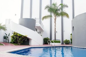 Un edificio moderno con piscina, palmeras y una estructura blanca curva.