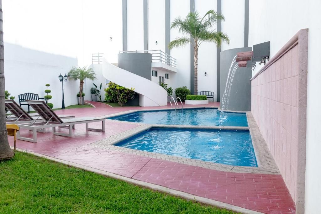 A swimming pool with a waterfall feature, surrounded by a red-tiled deck and lounge chairs.