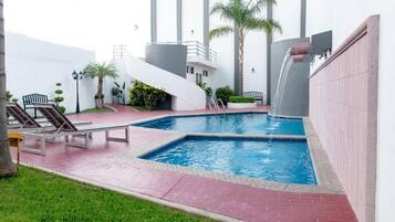 A swimming pool with a waterfall feature, surrounded by a red-tiled deck and lounge chairs.