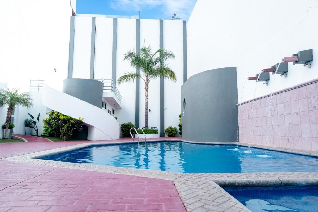 Ein Pool mit modernem Design, umgeben von einer gepflasterten Fläche mit einer Palme und einem Gebäude im Hintergrund, das eine markante, geschwungene Struktur aufweist.
