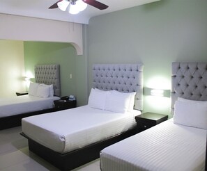 A hotel room with two beds, each with a tufted headboard and white bedding. There is a ceiling fan and a nightstand with a lamp between the beds. - Hotel Mirage (La Piedad)