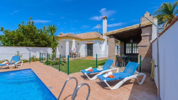 A pool area with lounge chairs, a barbecue area, and a white building with a tiled roof. - Casas Villanueva - Casa 2 Conil de la Frontera by Ruralidays (Cádiz)