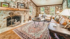 Una sala de estar acogedora con una chimenea de piedra, una mesa de centro redonda y un sofá de cuero.