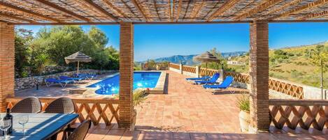 A poolside area with a view of the landscape, a table with chairs, and a pergola structure.