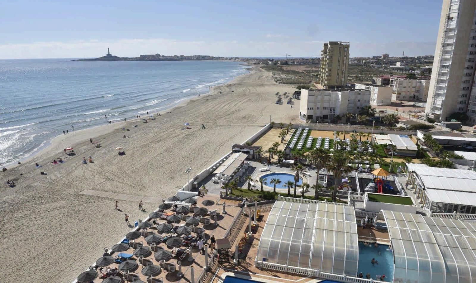 Un complejo turístico en la playa con piscina, sombrillas y vista al océano.