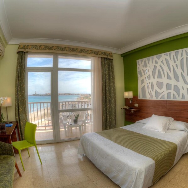 A hotel room with a bed, a desk, a chair, a balcony with a view of the sea, and a decorative wall panel.