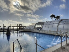 Ein Swimmingpool mit einer gläsernen Struktur, Palmen und einem bewölkten Himmel.