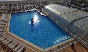 A swimming pool with a glass enclosure, surrounded by lounge chairs and umbrellas. - Hotel Spa Entremares (Cartagena)