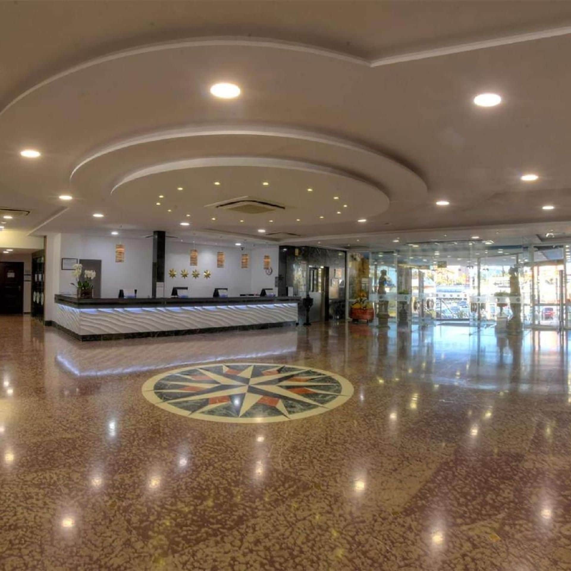 A spacious lobby with a reception desk, a decorative floor pattern, and a ceiling with recessed lighting.