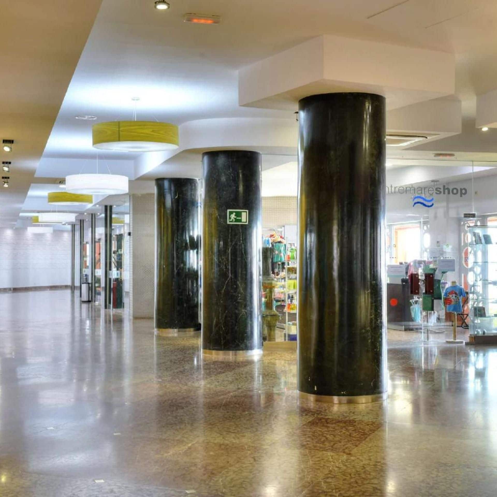 A spacious lobby with marble flooring and large black columns, leading to a shop area.