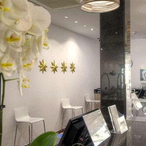 A reception area with a modern design, featuring a reception desk, white chairs, and decorative star-shaped wall art. - Hotel Spa Entremares (Cartagena)
