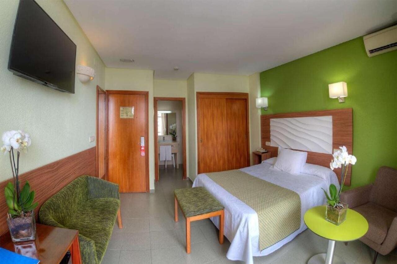 Una habitación de hotel con una cama, un escritorio, una silla, una mesita y un televisor.
