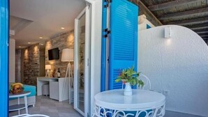 Una habitación con una mesa blanca, contraventanas azules y una pared de piedra.