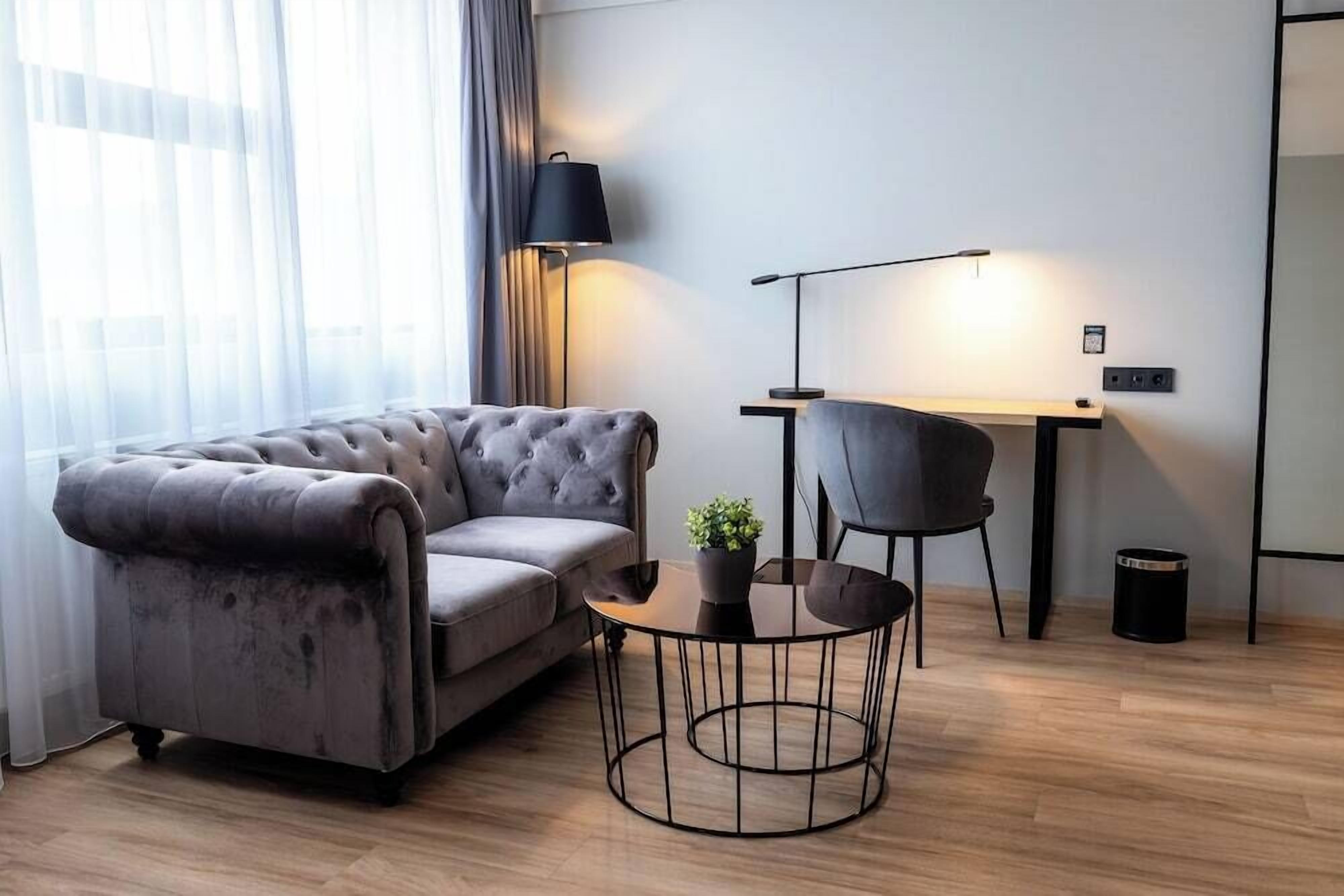 A modern living room with a grey sofa, a round coffee table, a desk, and a lamp.