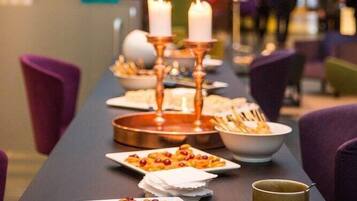 A dining area with a long table set for a meal, featuring candles and a variety of dishes.