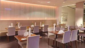 A modern restaurant with a warm ambiance, featuring neatly arranged tables with white tablecloths and chairs, and a soft, illuminated wall in the background. - Park Inn By Radisson Reykjavik Keflavik Airport (Reykjanesbær)