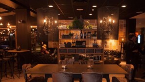 A restaurant with a long wooden table, cushioned chairs, and a central shelf with bottles and plants. - Park Inn By Radisson Reykjavik Keflavik Airport (Reykjanesbær)