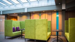 A modern indoor seating area with green upholstered chairs and a small table, featuring a skylight and wooden panel walls. - Park Inn By Radisson Reykjavik Keflavik Airport (Reykjanesbær)
