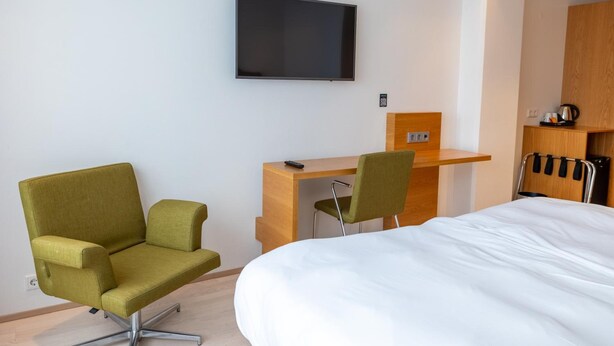 A hotel room with a bed, a desk with a chair, a television on the wall, and a wooden cabinet. - Park Inn By Radisson Reykjavik Keflavik Airport (Reykjanesbær)