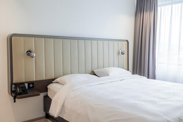 A hotel room with a bed, a bedside table with a phone, and a window with curtains. - Park Inn By Radisson Reykjavik Keflavik Airport (Reykjanesbær)