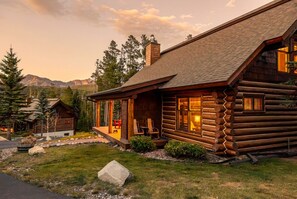 A log cabin with a porch, a chimney, and a view of mountains. - Platinum Big Sky Log Cabin | Ski-In/Out, Hot Tub, 2 King Suites & Arcade (Big Sky)