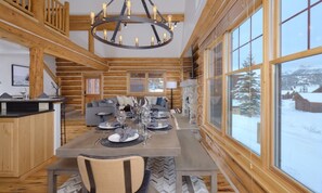 L’intérieur d’une cabane en rondins comprend un coin repas, des murs en bois, de grandes fenêtres et un lustre.