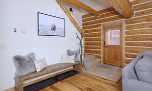 A log cabin interior with a wooden bench, a door, and a framed picture on the wall.
