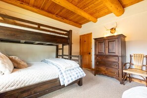 A bedroom with a wooden bunk bed, a wooden dresser, a chair, and a door.