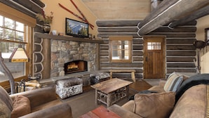 A log cabin interior with a stone fireplace, leather furniture, and ski equipment on the wall. - BIg Sky Vacation Rentals: PR Manitou 15 (Big Sky)
