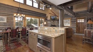A log cabin interior with a dining area, kitchen, and stone fireplace. - BIg Sky Vacation Rentals: PR Manitou 15 (Big Sky)