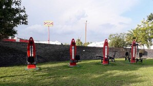 Four red exercise machines on a grassy area with a stone wall and a sign in the background.