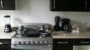 A kitchen with a gas stove, pots, a coffee maker, and a blender.