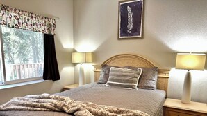 Une chambre à coucher comprenant un lit, deux tables de chevet avec des lampes, une fenêtre avec des rideaux et une œuvre d’art accrochée au mur.