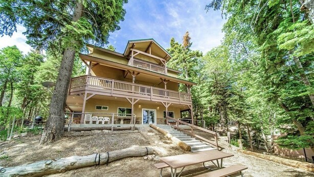 Un chalet à deux étages doté d’un balcon, entouré d’arbres.
