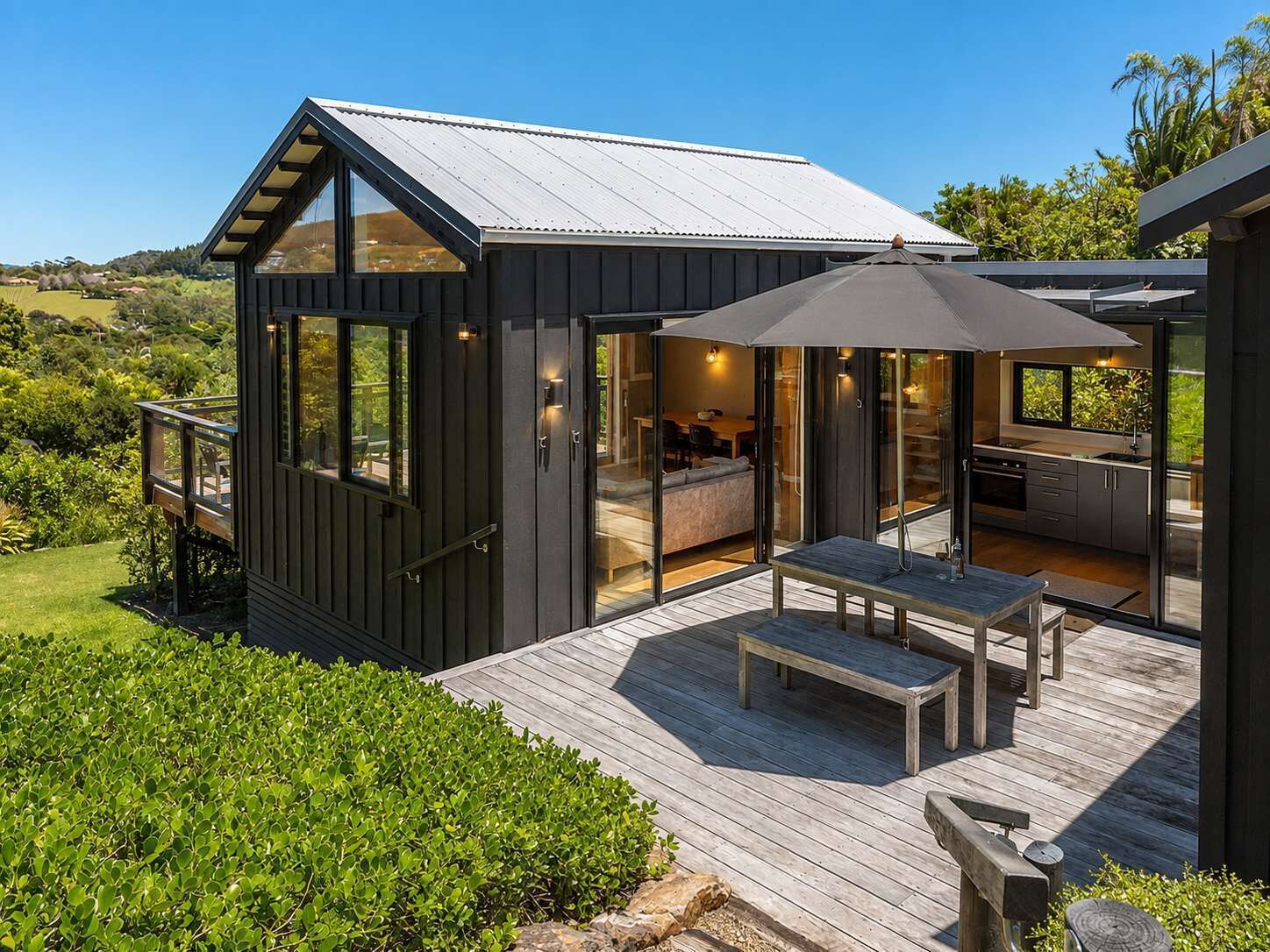 Una casa moderna con una terraza, un comedor y una cocina visibles a través de puertas de vidrio.