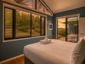 A bedroom with a large window, a bed, a chair, and a view of greenery.