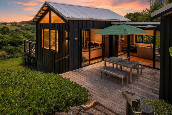 A modern house with a deck, a dining area, and a kitchen visible through large glass doors.
